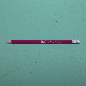 An image showing a promotional pencil on a paper texture background. The background is blue and the pencil is maroon with the DS Creative logo printed on the side